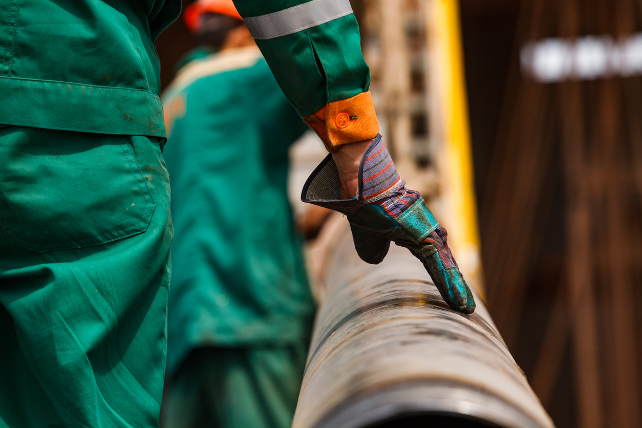 Two oil workers in green and orange work wear and work gloves and rusted drilling pipe. Close up of one worker's hand. Low depth-of-field. Oil deposit in Kazakhstan